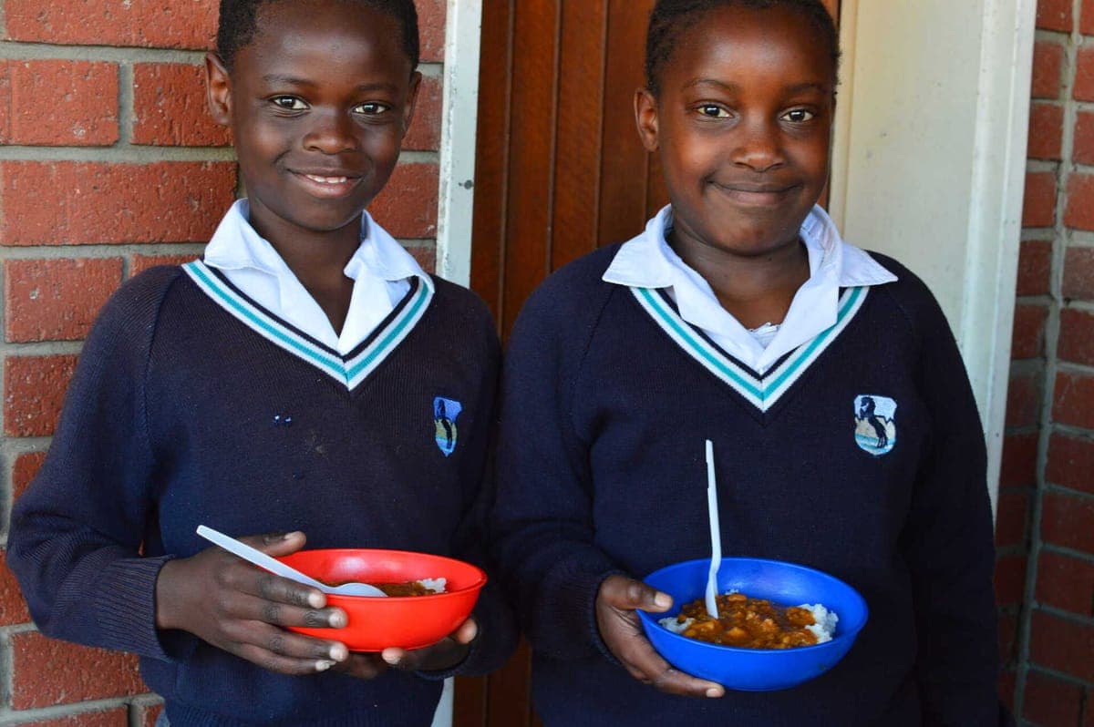 Two smiling children from the SALT School Feeding Programme holding bowls of lunch